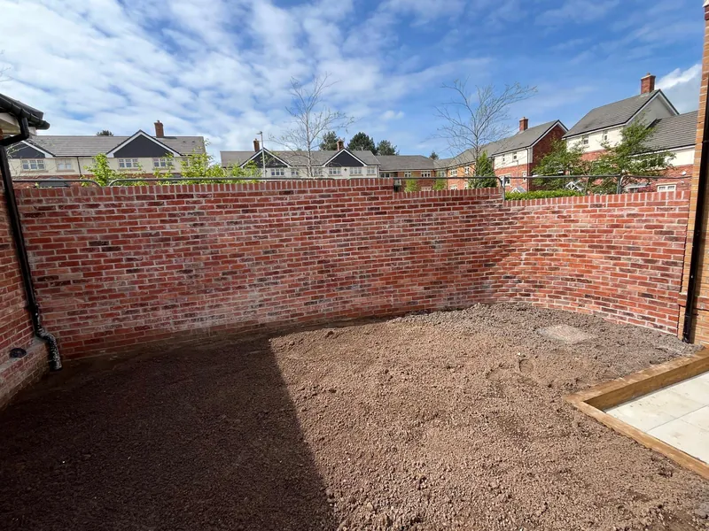 A tall red brick boundary wall enclosing a newly levelled garden.