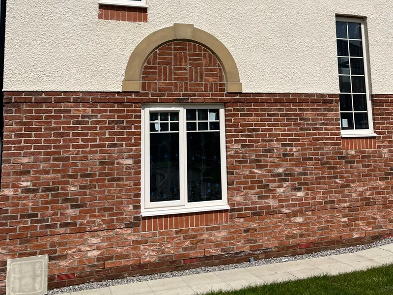 Brickwork with an arched panel of patterned bricks above a window on a new home.