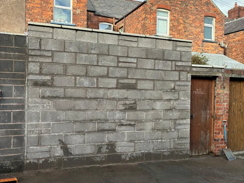 A new block boundary wall beside a rear lane, next to a timber door.