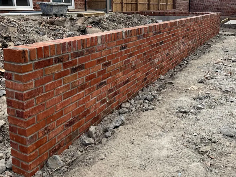 A long run of new red brick garden wall with a brick-on-edge top.