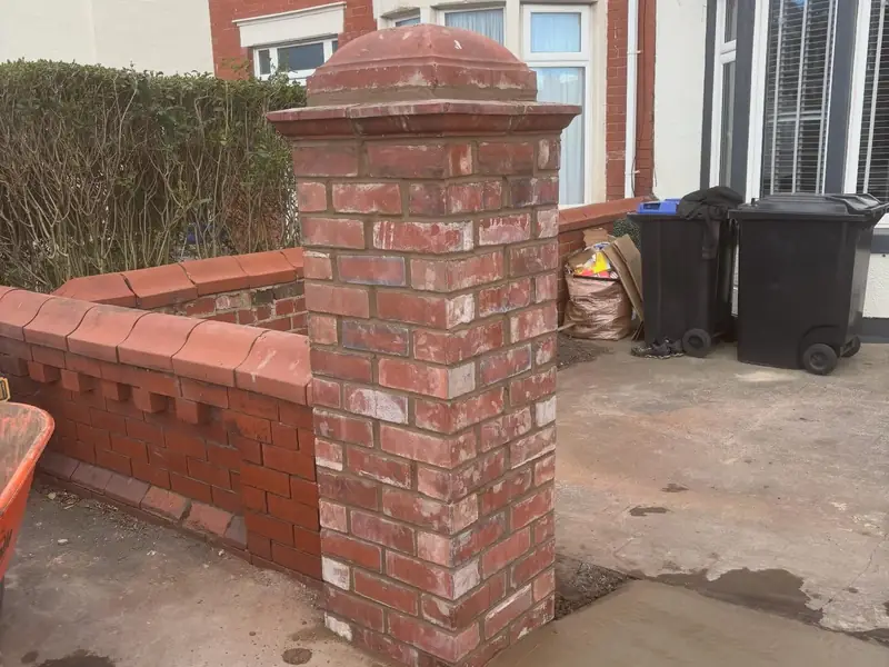Red brick gate pier with a stone cap, beside a matching low brick front garden wall.