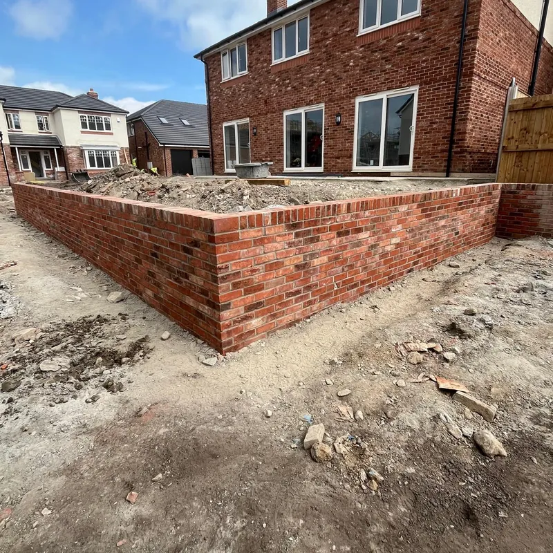 A new red brick garden wall turning a corner, with a brick-on-edge top.