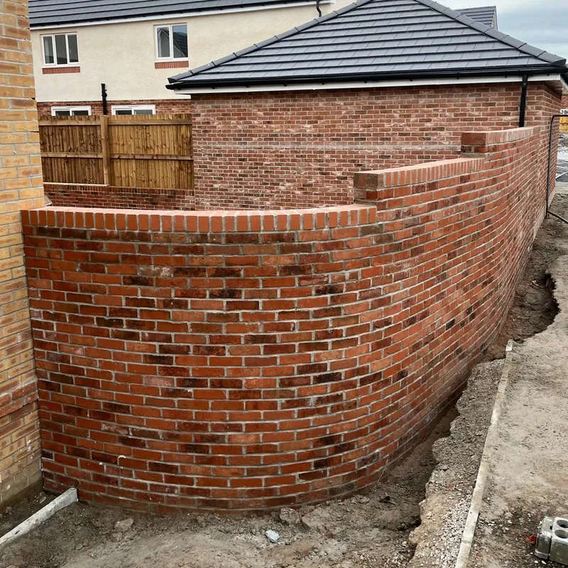 A curved red brick wall with a brick-on-edge top, built beside a new home.