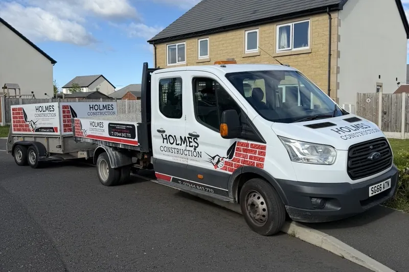 Holmes Construction branded work van and trailer parked outside a house.