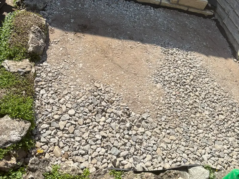 Crushed-stone sub-base spread across a garden area ready for paving, with new walling at the far end.