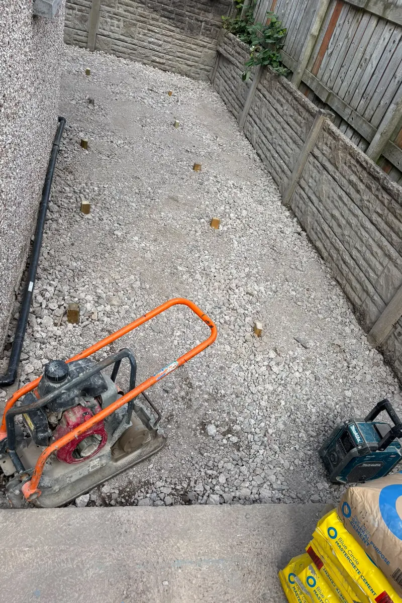 The same side garden with a compacted crushed-stone sub-base and a plate compactor.