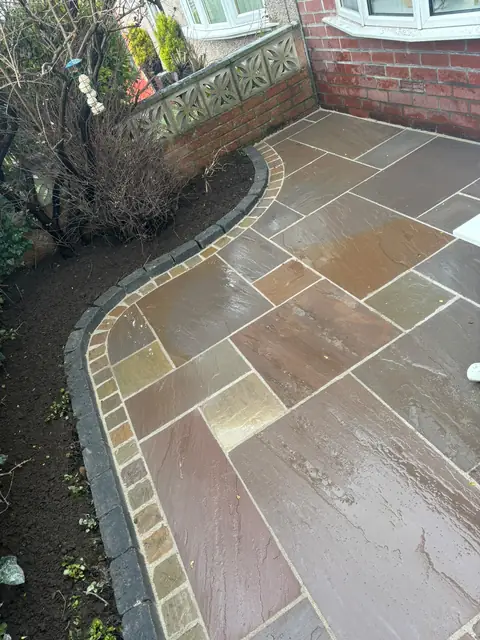 Natural stone patio with a curved edge of contrasting setts beside a planted border.