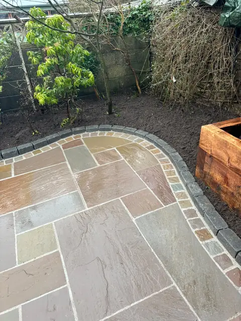 Curved patio edge separating the paving from a planted border, with a timber sleeper raised bed.