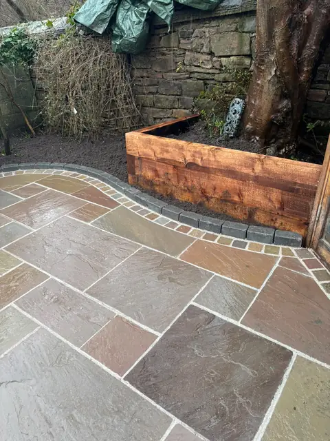 Paved patio with a curved sett edge beside a timber sleeper raised bed.