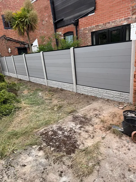 A long run of grey slatted fence panels between concrete posts along a garden boundary.