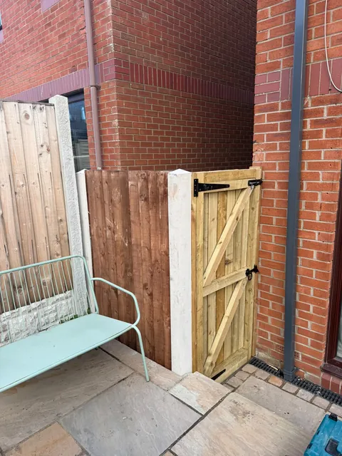 A timber side gate with black hinges beside a fence panel and concrete post.