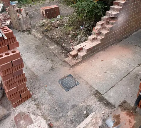 The new brick wall partly built, with bricks stacked ready to use.