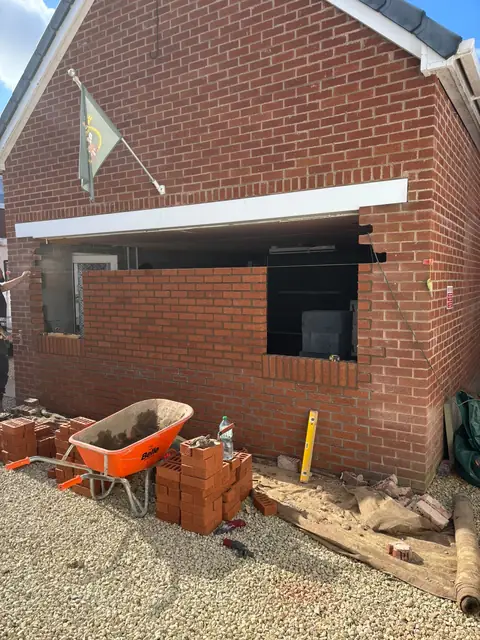 The new brick front wall partly built, with bricks and a wheelbarrow on the driveway.
