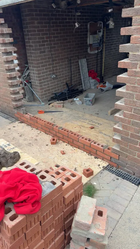New brickwork being laid across the base of a former garage door opening, with the old brickwork cut back either side.