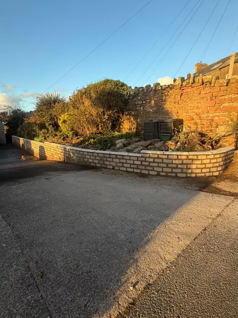 Newly built curved garden wall in pale facing bricks along the edge of a raised garden bed.