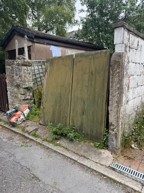 Rotten timber gates between deteriorating stone and rendered piers.