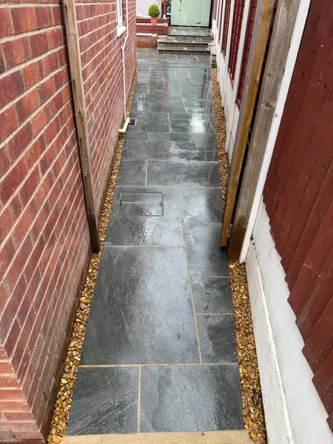 A paved side passage between the house and a timber wall.