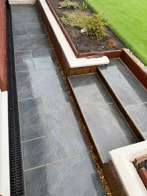 Grey paving with steps alongside raised beds.