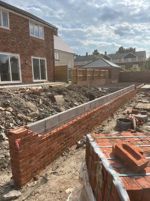 The red brick wall partly built, with a block inner wall behind it and bricks stacked nearby.