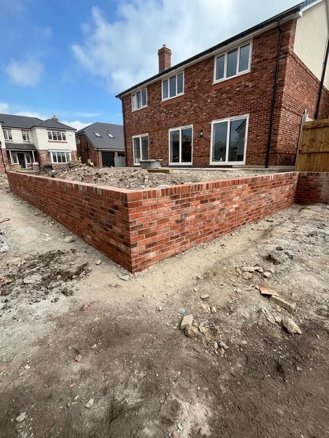 The finished red brick wall turning a corner, with a brick-on-edge top.