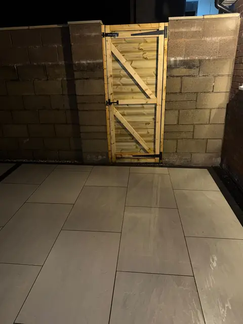 Finished pale paving in front of a timber gate set in a block wall.