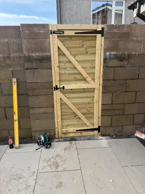 Timber ledged and braced gate hung in a block wall, above the new paving.