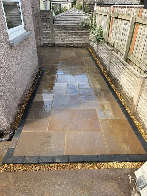 The same side garden with new natural stone paving, a dark block border and gravel edging.