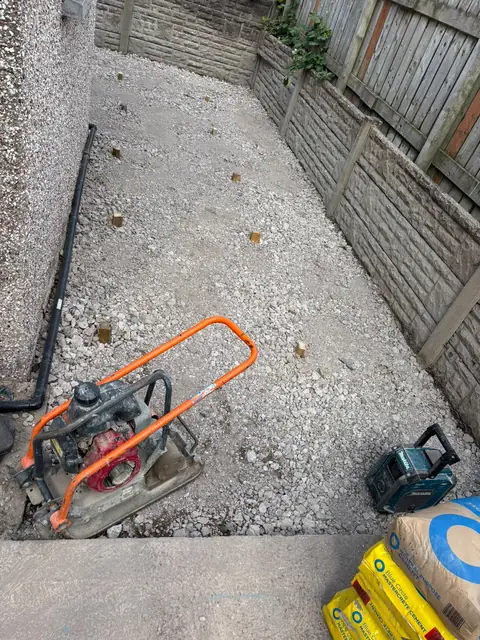 The side garden with a compacted crushed-stone sub-base and a plate compactor.