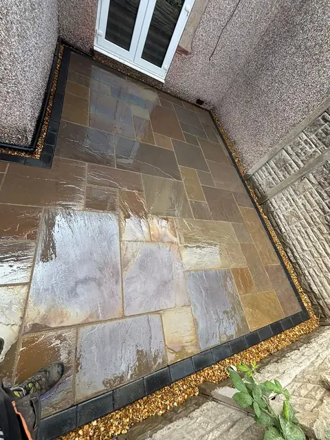Natural stone paving in a side garden beside the house, with a dark block border.