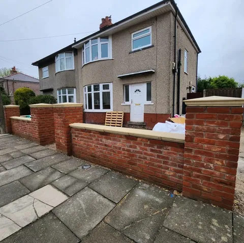 A red brick front garden wall with brick piers and pale coping stones outside a semi-detached house.