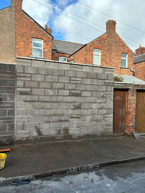 A new block boundary wall beside a rear lane, next to a timber door.