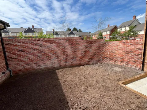 A tall red brick boundary wall enclosing a newly levelled garden.