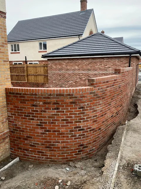 A curved red brick wall with a brick-on-edge top, built beside a new home.