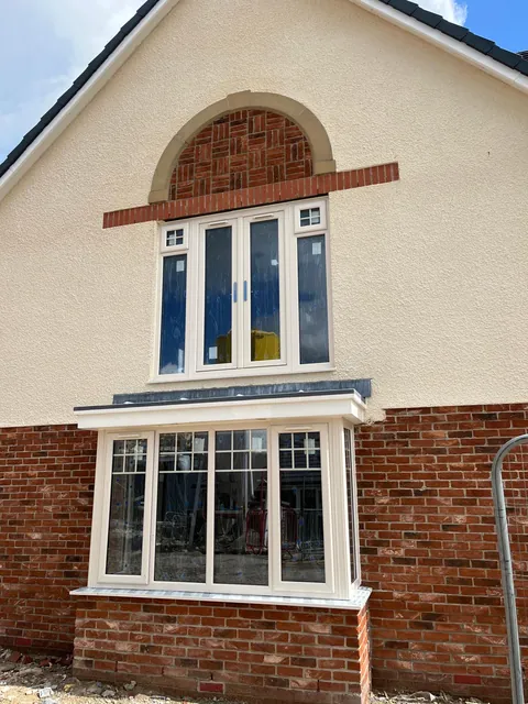 The gable of a new home with an arched panel of patterned brickwork above the upper windows and red brickwork around a bay window.