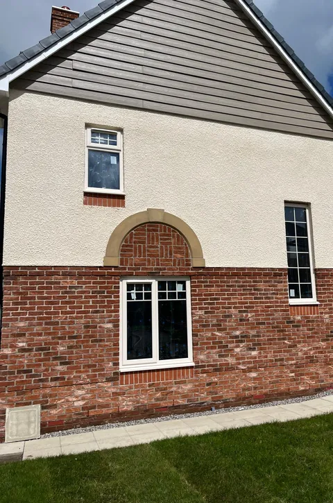 Red brickwork on a new home with an arched panel of patterned bricks above a window.