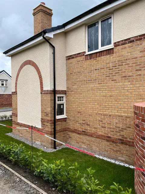 The side of a new home with a red brick arch and red brick bands contrasting with buff brickwork.