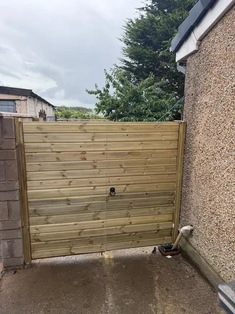 A pair of horizontal-board timber gates with a ring handle, between a block wall and a rendered house.