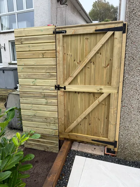 A ledged and braced timber gate with black hinges beside a horizontal-board fence panel.