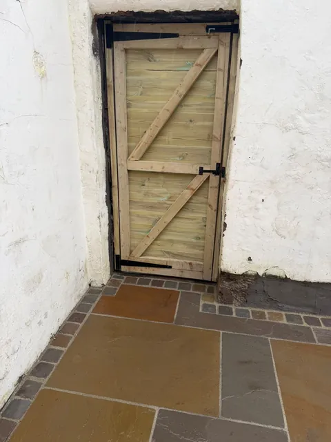 A ledged and braced timber gate fitted in a doorway in a white-painted wall, above natural stone paving.