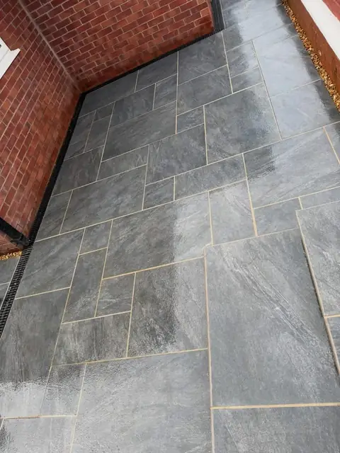 Grey stone-effect patio laid in a random pattern, with a drainage channel along the house wall.