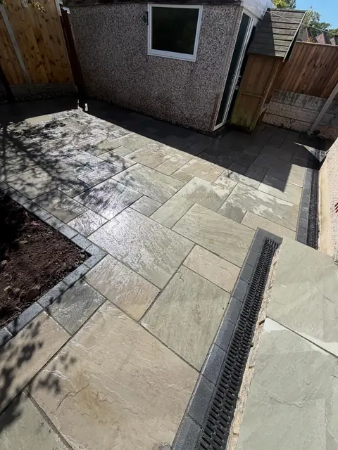 Natural stone paving with a channel drain and a planting border edged in dark blocks.