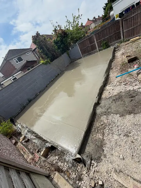 Freshly laid concrete base along a garden boundary wall.