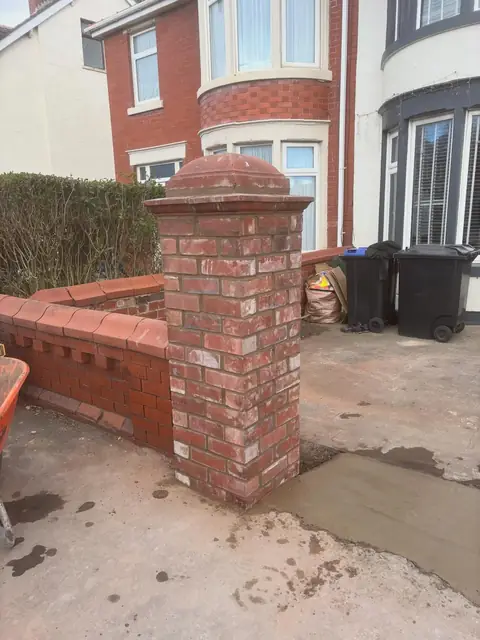 Red brick gate pier with a stone cap, beside a matching low brick front wall.