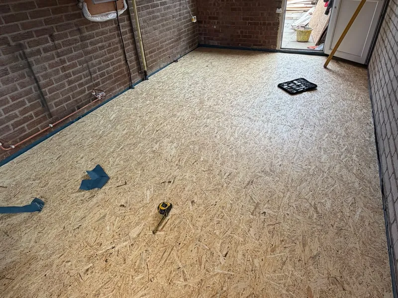 New floor boarding laid across a garage being converted, with brick walls still bare.