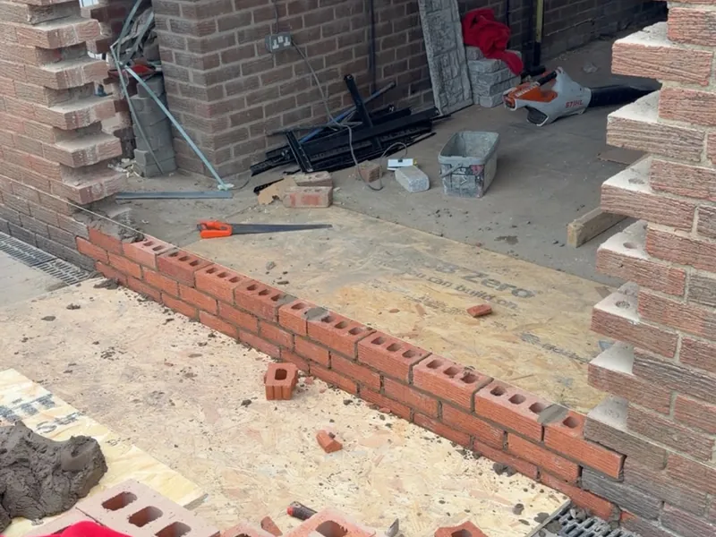 New brickwork being laid across the base of a former garage door opening, with the old brickwork cut back either side.