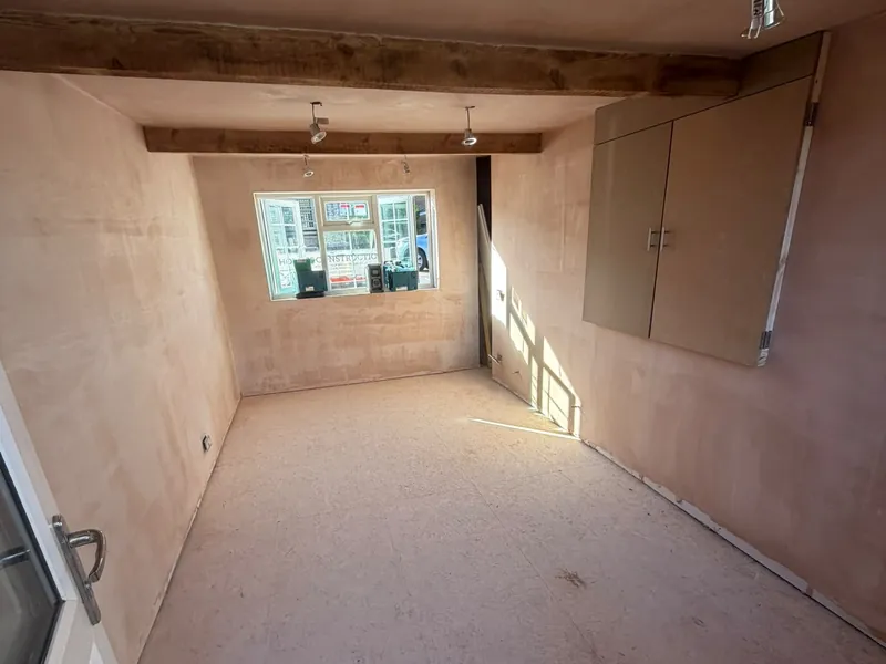 The converted garage after plastering, with exposed timber beams and a fitted cupboard.