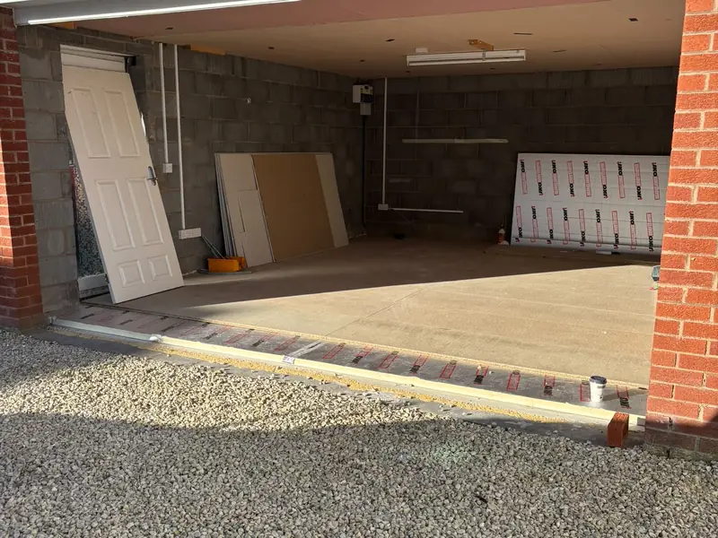 Inside a garage at the start of a conversion, seen through the open doorway, with block walls and building materials stacked inside.