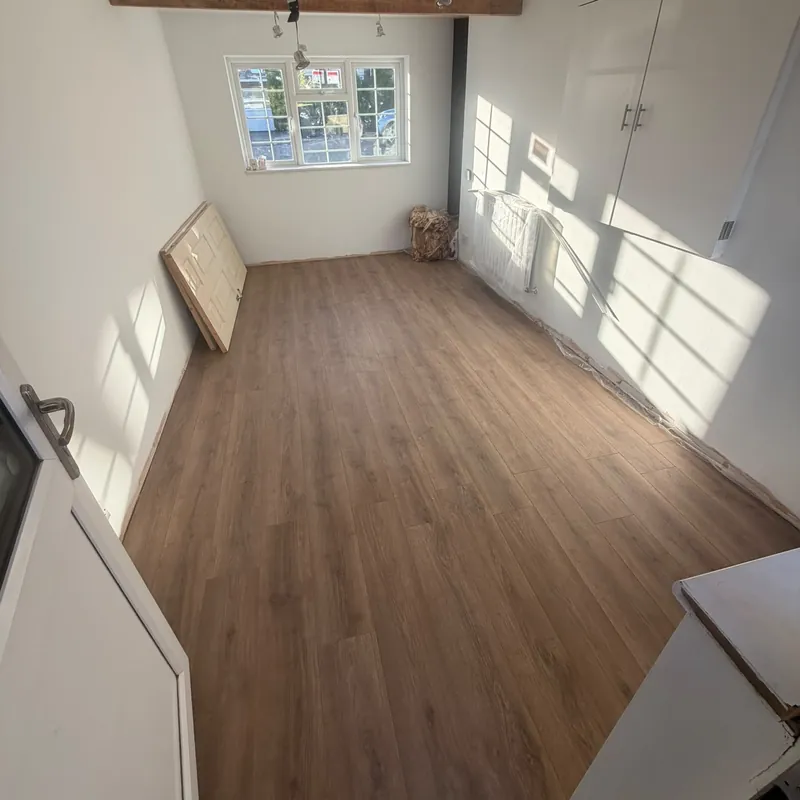 A converted garage room with white walls, exposed timber beams, ceiling spotlights and wood-effect flooring.