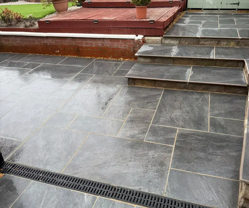Grey stone patio with new steps up to a raised level and a drainage channel