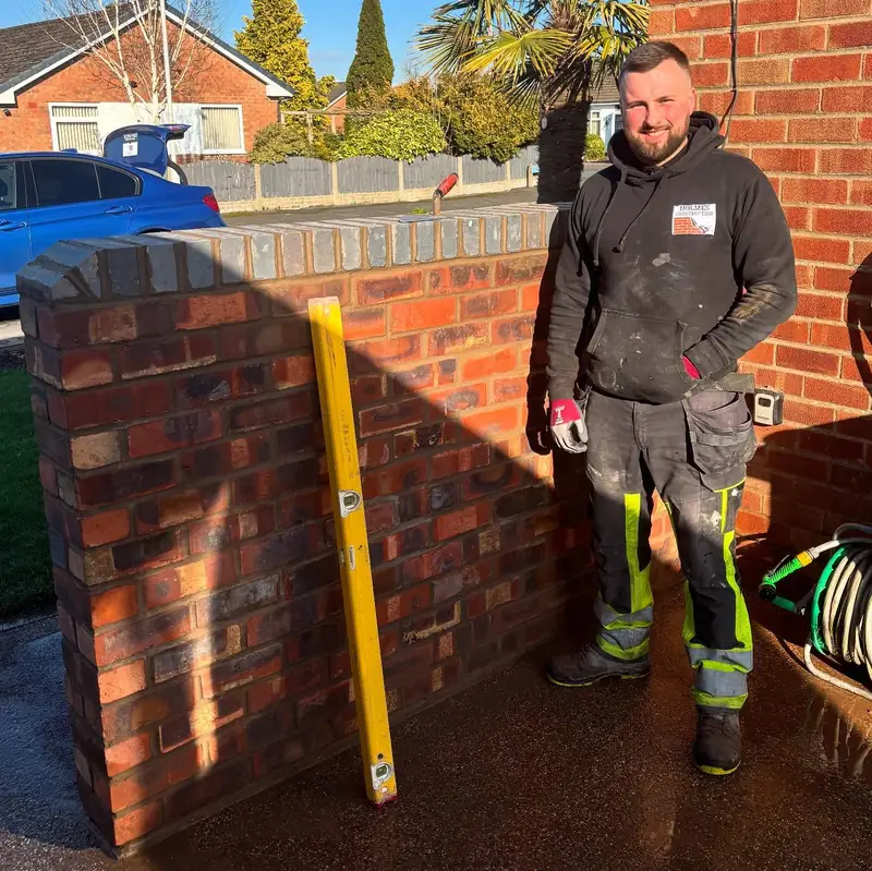 Lewis of Holmes Construction beside a newly built brick garden wall.